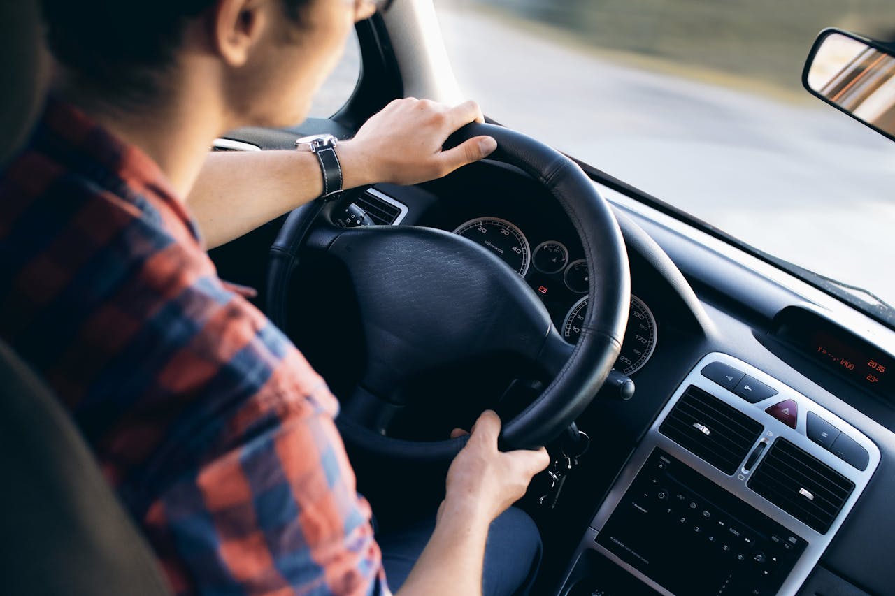 A man sitting behind the wheel of a car and driving on the road.