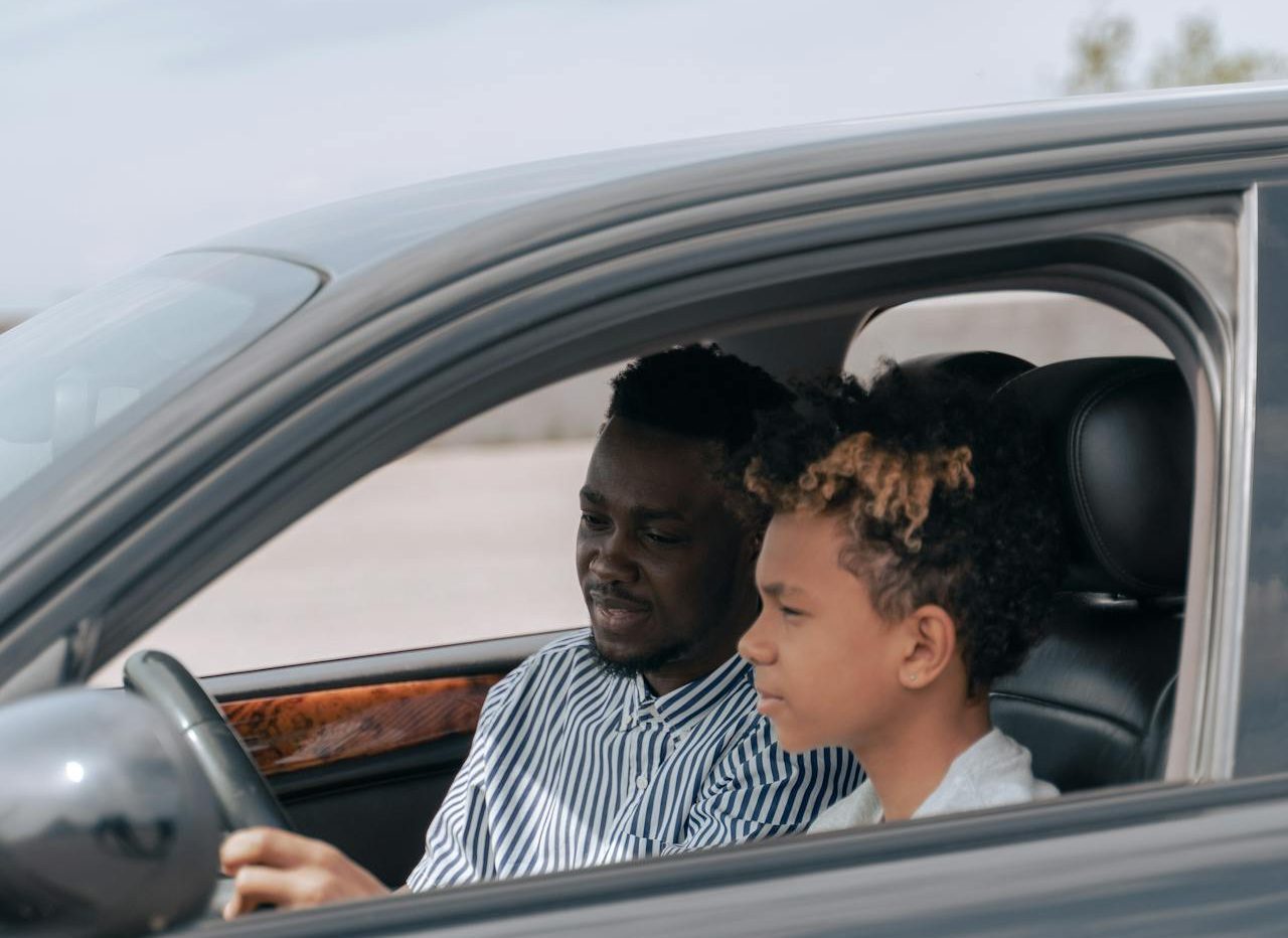 A teenager learning how to drive with his father by his side.