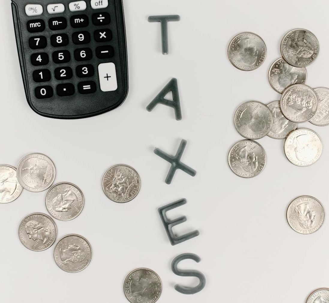 Coins and a calculator spread out on a white surface. There are also letters that spell out the word "TAXES".